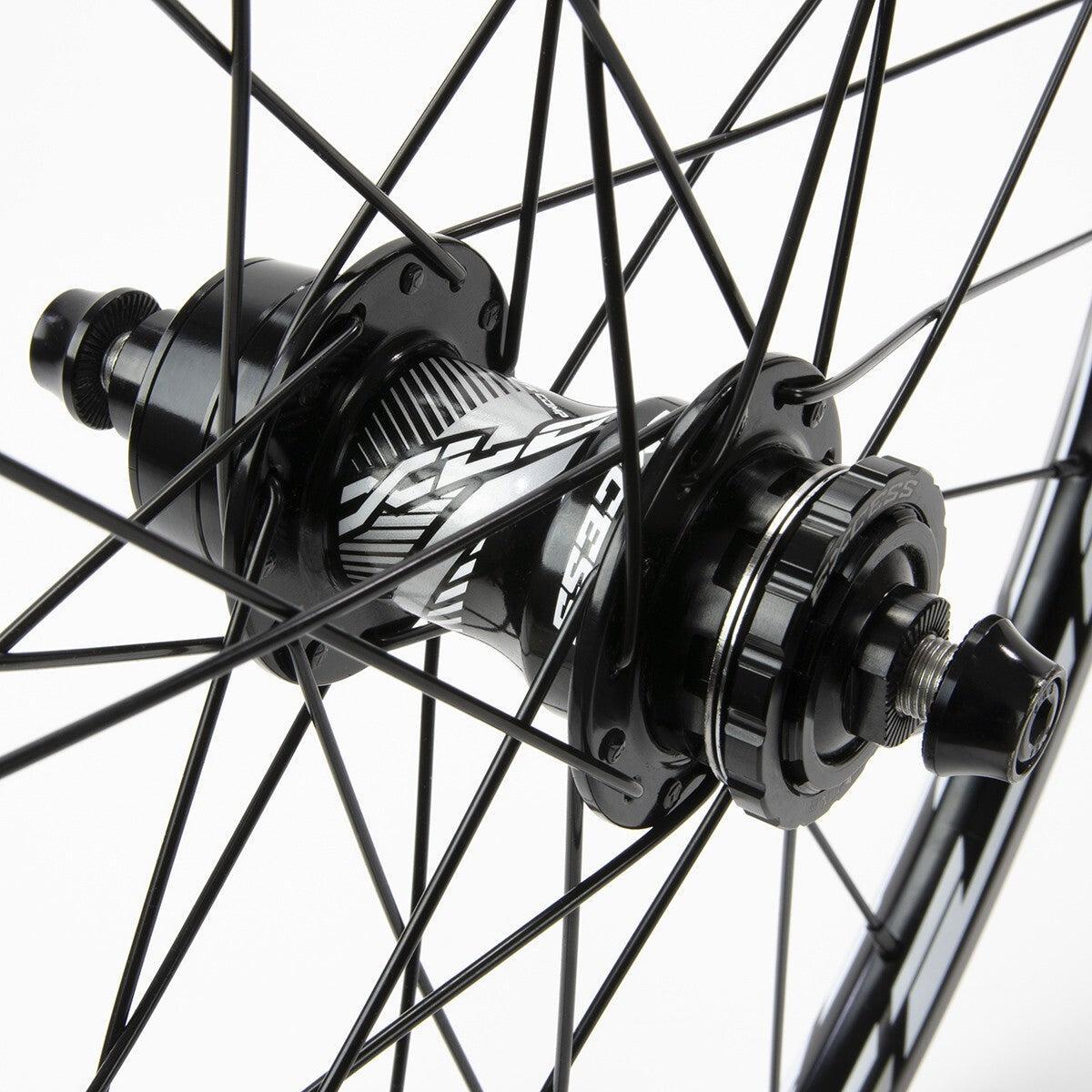 Close-up of the Excess XLC-2 20 x 1.3/8 Alloy Wheel Set 36H hub, featuring a black finish, patterned design, and visible axle bolts with spokes radiating outward.