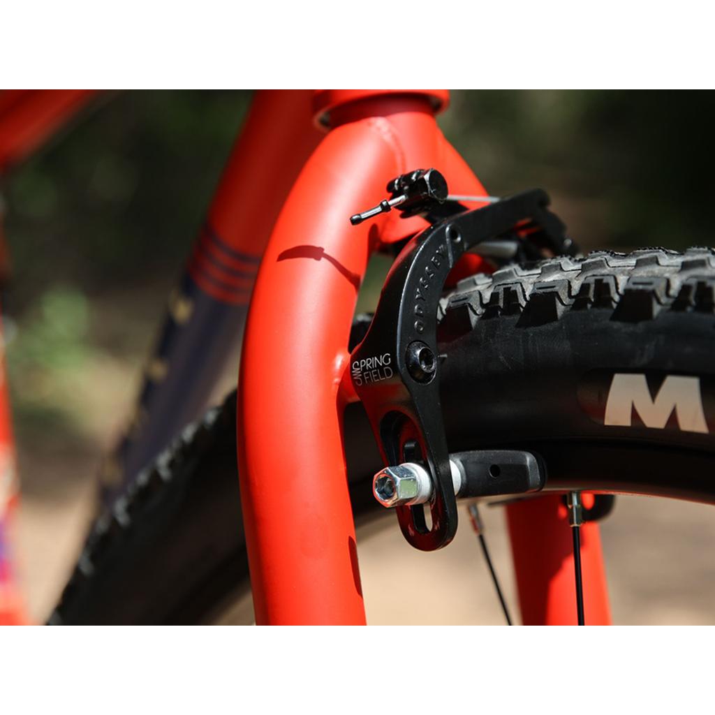 Close-up of a red Fairdale Taj 27.5 Inch Bike (2023) frame, featuring a mounted brake caliper on a knobby tire—ideal for riders wanting a tough single speed or BMX-style commuter setup.