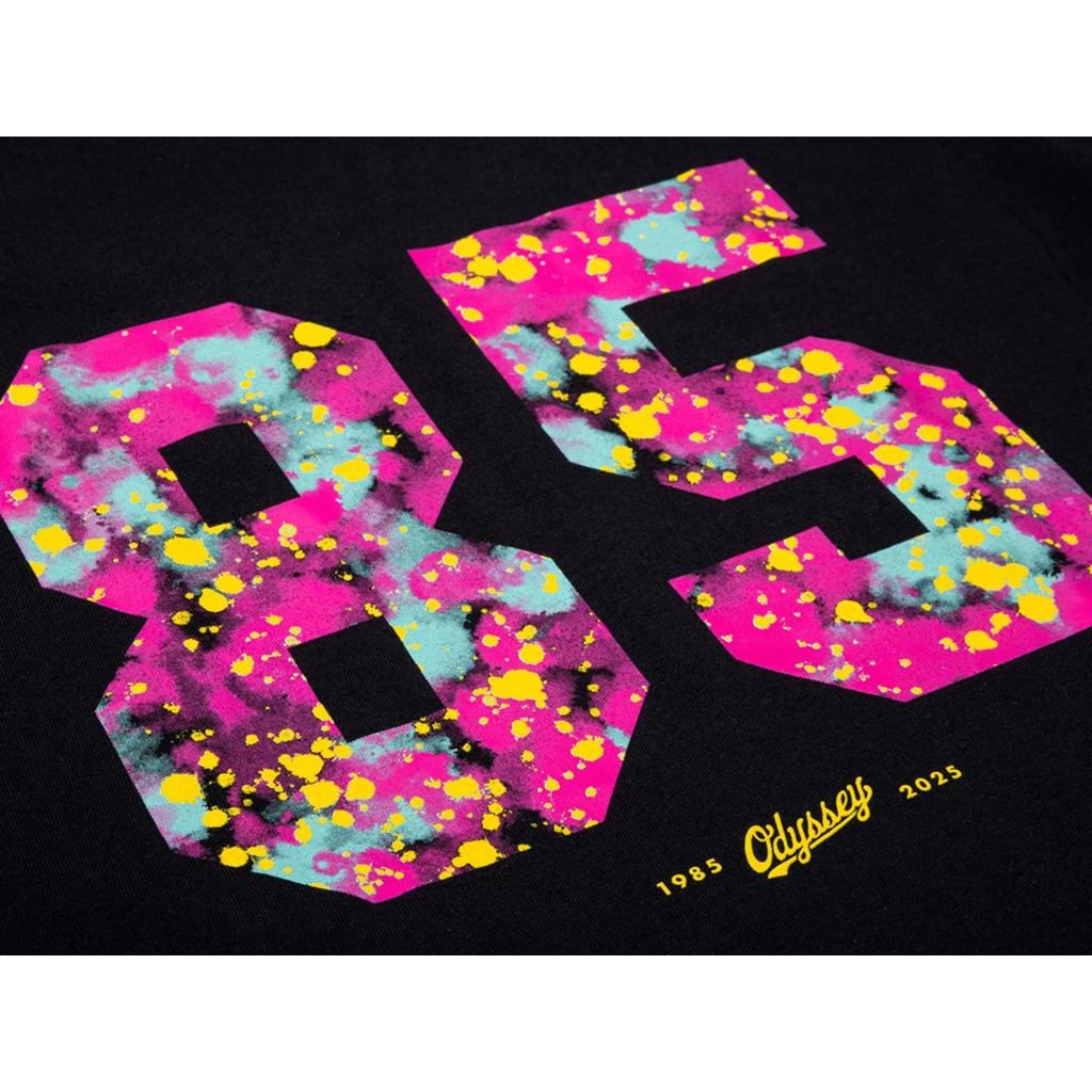 The Odyssey 85 Splatter T-Shirt features a bold, colorful "85" with a striking splatter effect. "Odyssey" and the years 1985 and 2025 are highlighted in yellow below, making this tee an eye-catching choice.