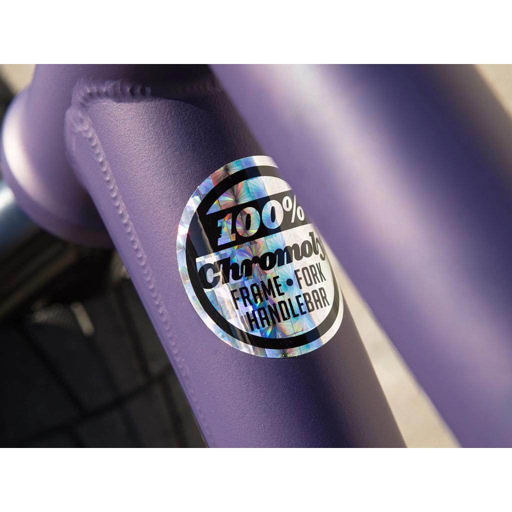 Close-up of a holographic sticker on the Sunday Dark Wave Authentic 20 Inch Bike’s purple frame reads “100% Chromoly FRAME FORK HANDLEBAR,” showcasing the signature model’s quality construction.