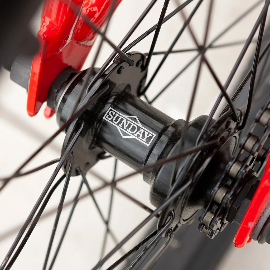 A close up of a red Sunday Blueprint 20 inch Bike wheel with black spokes.