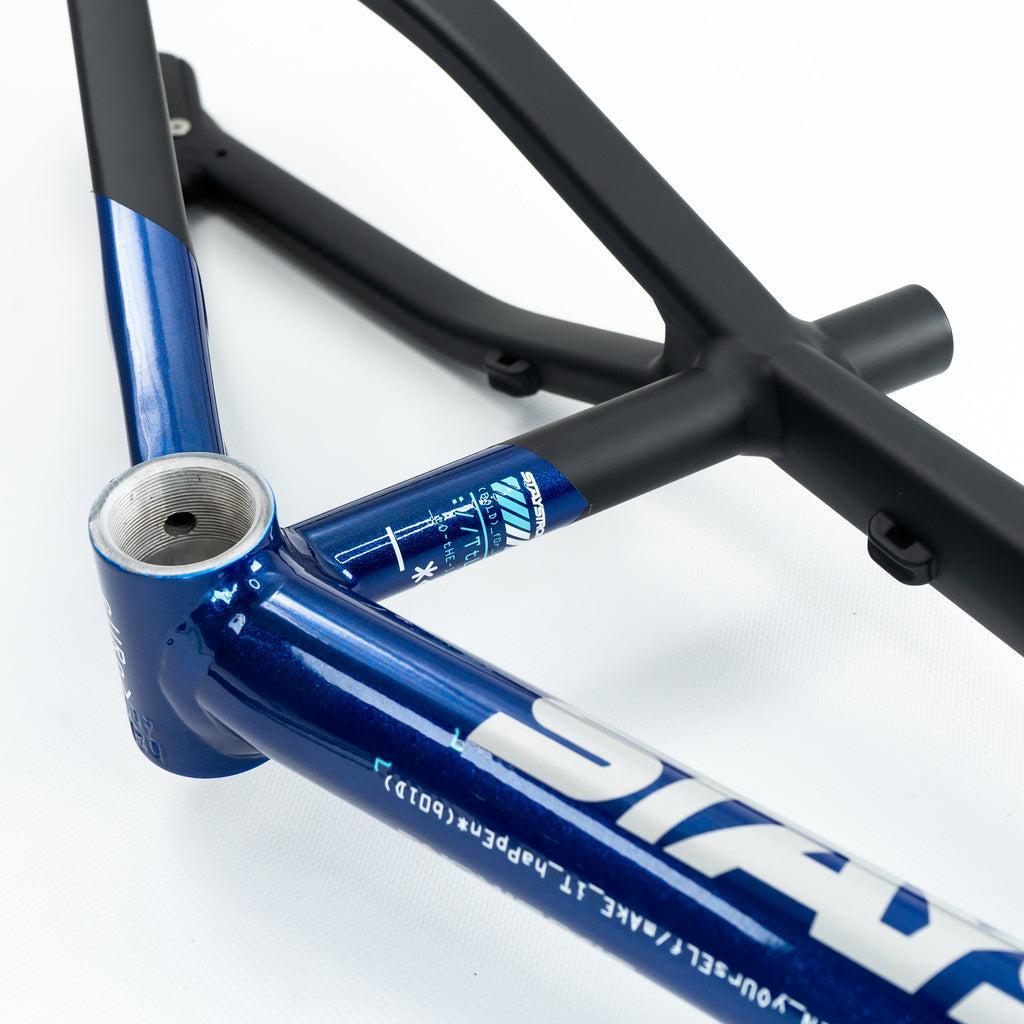 Close-up of the Staystrong V5 Disc Junior Frame, showing a glossy blue 6061 alloy front triangle with white graphics and text, seamlessly joined to a matte black rear triangle, displayed against a white background.