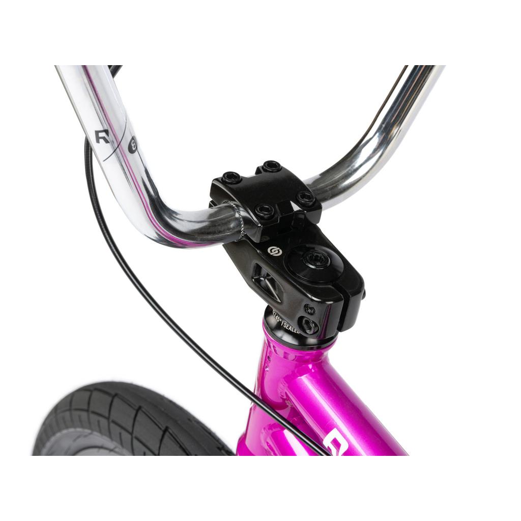 Close-up of the handlebar and stem on a Radio Saiko 20 Inch Bike, showing its bright pink BMX frame, part of the front tire with Salt Tracer Tyres, and a visible brake cable.