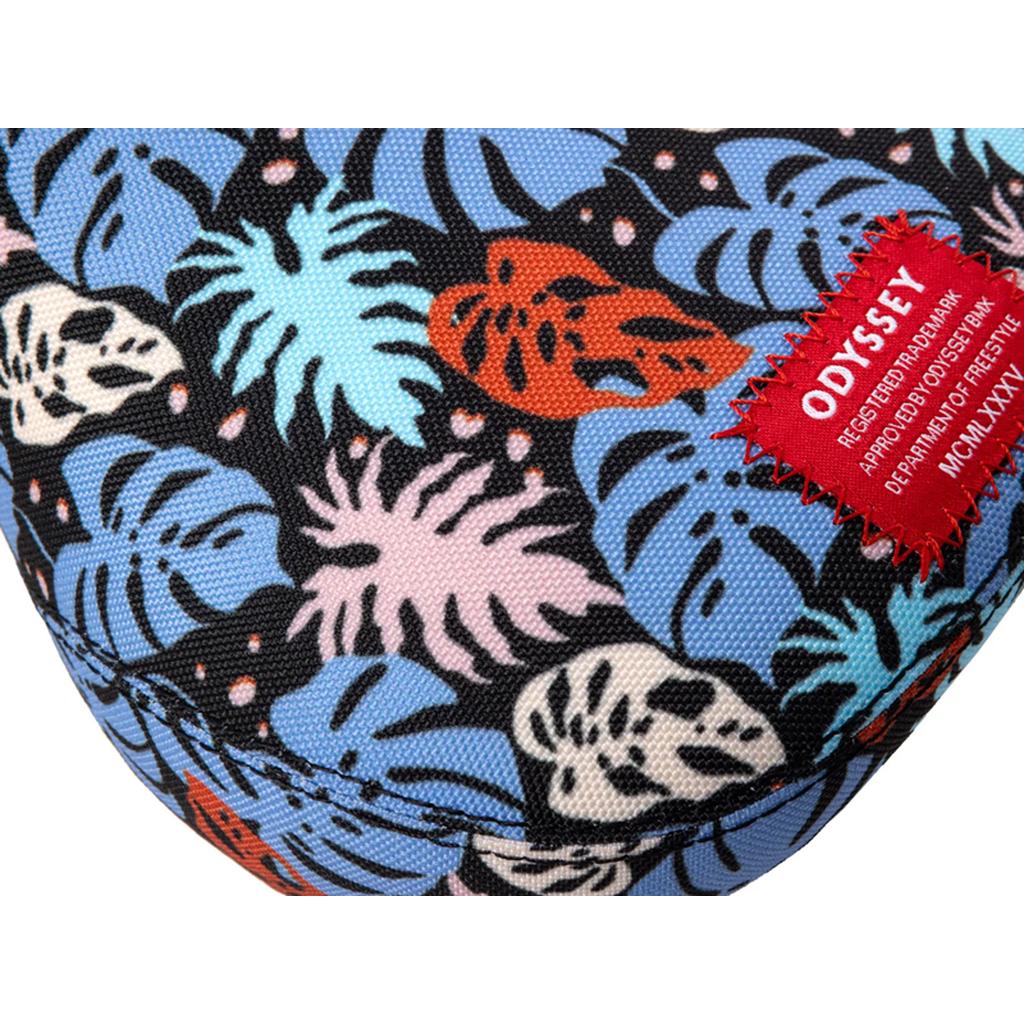 Close-up of the Odyssey Tropical V1 Pivotal Seat featuring a vibrant fabric with blue, orange, pink, and black tropical leaf patterns. A red sewn label reads "ODYSSEY" amid colorful sublimated artwork, radiating tropical vibes.