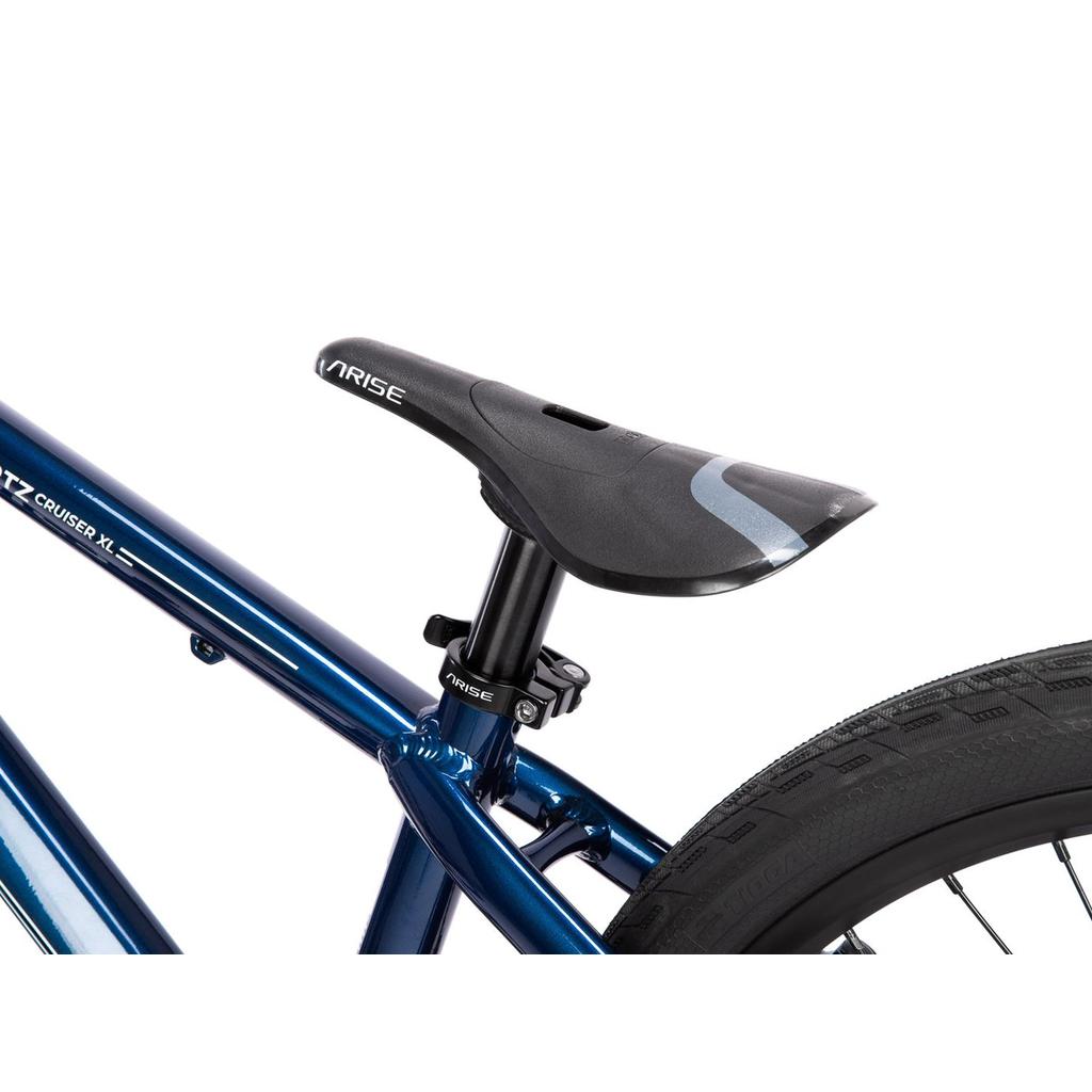 Close-up of a black V-Rise saddle on a metallic blue Radio Raceline Quartz Pro Disc 24 Inch Bike, showcasing the seat post and rear tire of this lightweight, race-ready cruiser.