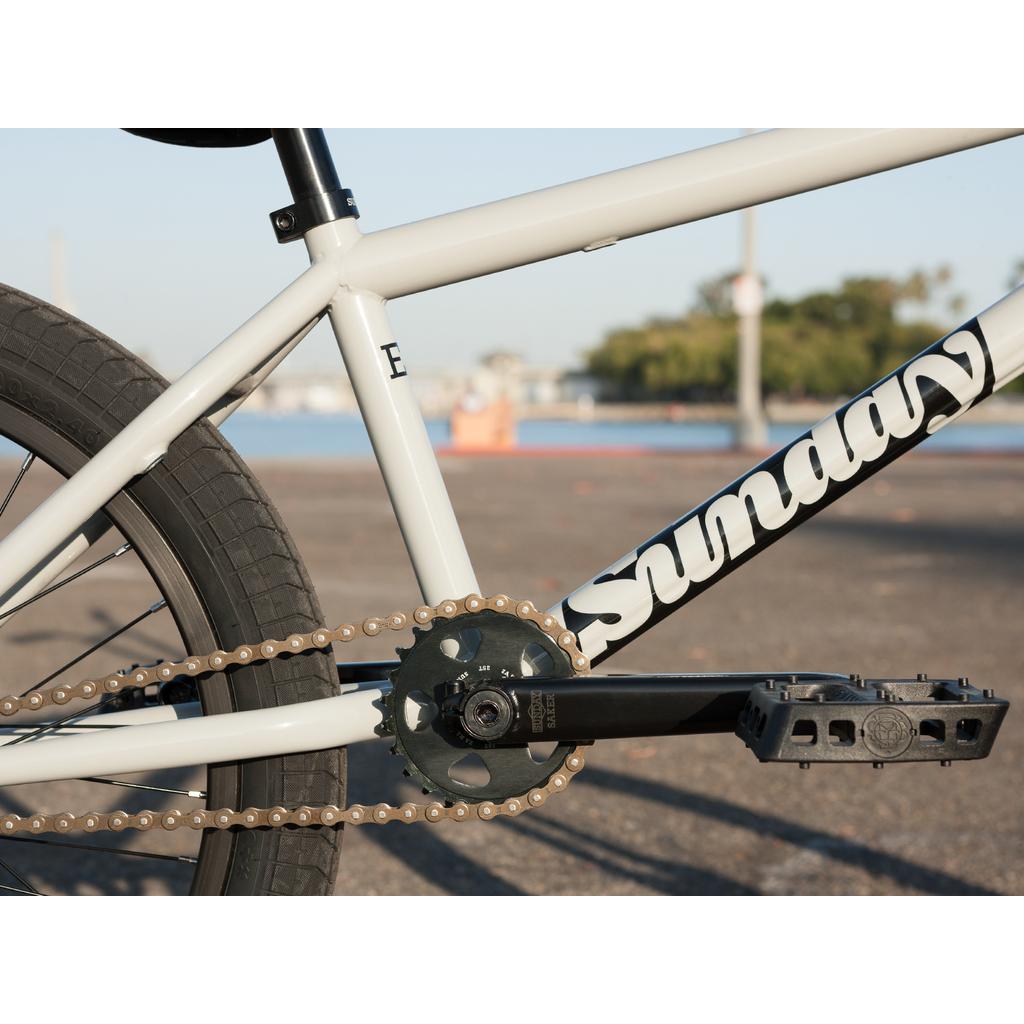 Close-up of the Sunday EX Erik Elstran 20 Inch Bike, showing its 100% chromoly frame, "Sunday" logo, rear wheel, chain, crankset, and pedal in an outdoor setting.