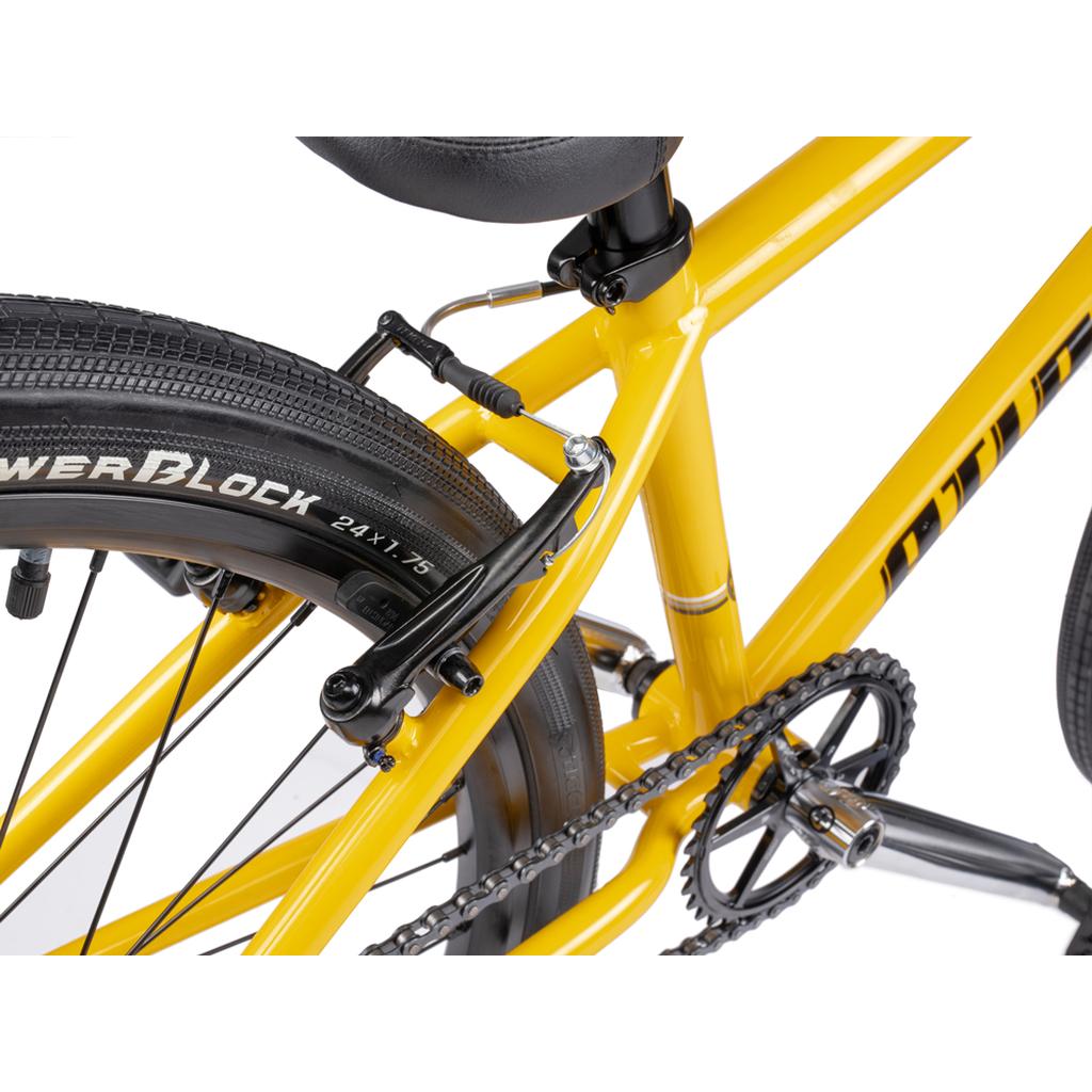 Close-up of the rear section of a yellow Wethepeople Atlas 24 Inch Bike, showcasing its seat, 24" wheels, tires, frame, brake system, and parts of the chain and pedal.