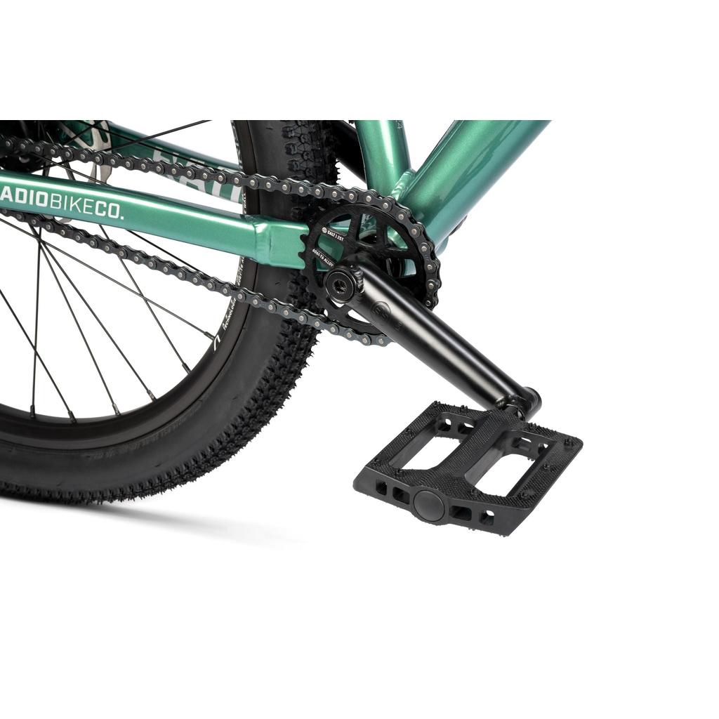 Close-up of the Radio Griffin 24 Inch Dirt Jumper Bike's rear wheel, chain, crank arm, and flat pedal, with a section of the green frame in view.