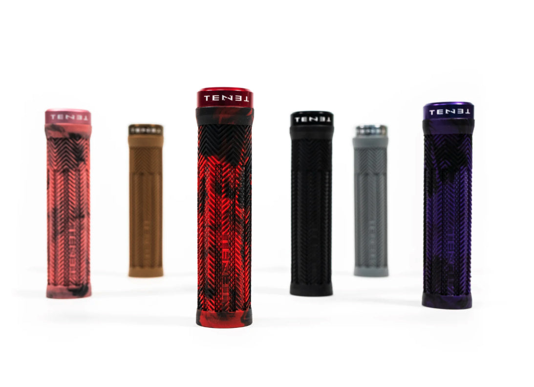 Six Tenet Components Icon Grip mountain bike grips in assorted colors—red, brown, black, gray, and purple—are arranged upright on a white background. Designed with extra-soft rubber for optimal comfort and control, these lock-on grips ensure a secure fit for every ride.
