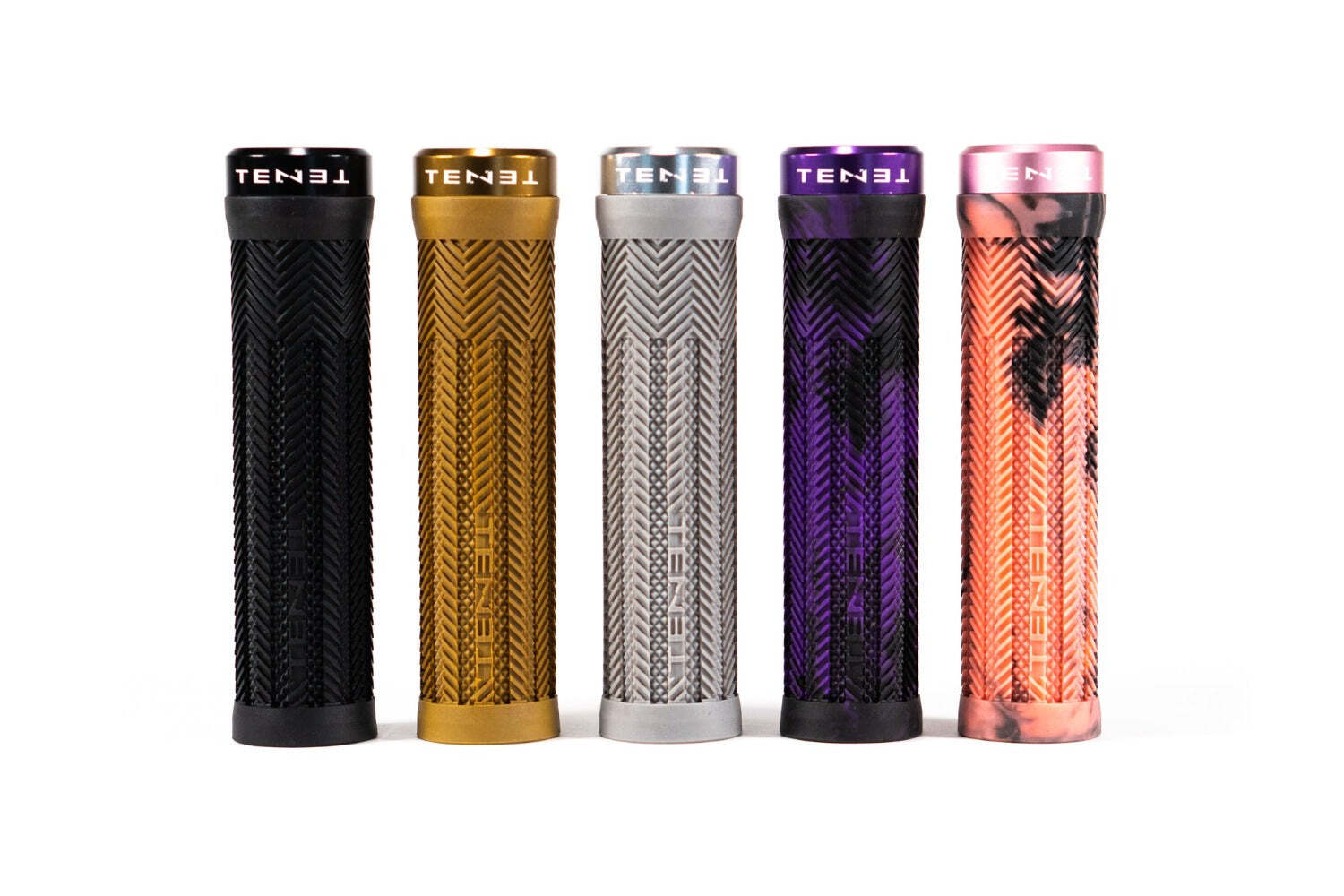Five Tenet Components Icon Grip textured cylindrical mountain bike grips, in black, gold, silver, purple, and pink camouflage, stand upright side by side on a white background. These extra soft rubber grips are designed for superior comfort and control.