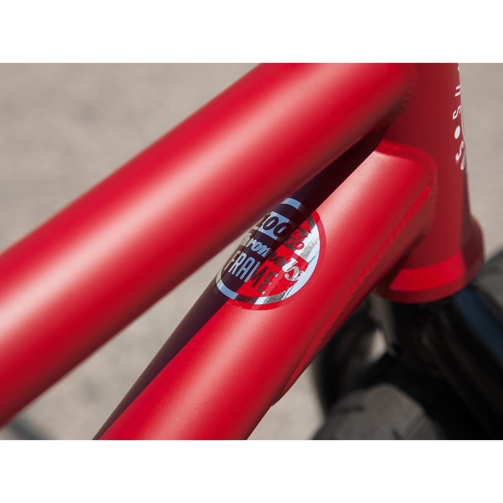 Close-up of a Sunday Forecaster 20 Inch Bike's red frame with a "100% Chromoly Frame" sticker, plus black tire and Odyssey parts in the background.