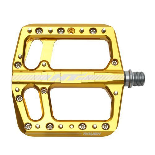 The HT Components ANS12 Raven Pedals feature a gold-colored aluminum body with multiple grip pins, a wide open design, and a visible right-side axle attachment for secure mountain bike use.