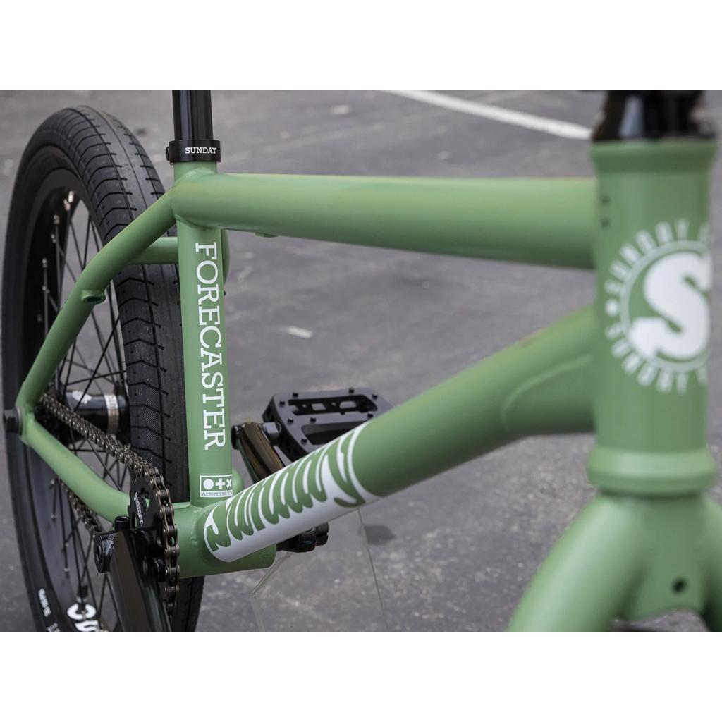 Close-up of a green Sunday Forecaster 20 Inch Bike (2025) / Brett Silva BMX with a full chromoly frame, black pedals, chain, and tires, parked on pavement.