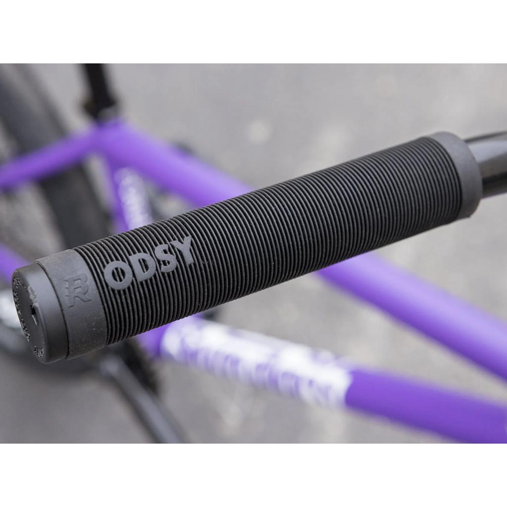 Close-up of a black bicycle handlebar grip with "ODSY" text, attached to a purple Sunday Forecaster 20 Inch Bike frame in the background, featuring quality Odyssey parts.