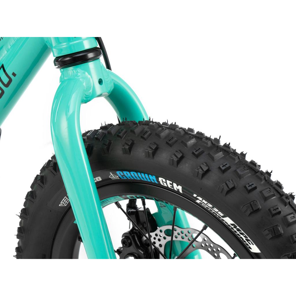 Close-up of the Radio Zuma 14 Inch Bike shows its turquoise front fork and wide, knobby fat tire with white branding—ideal for a lightweight, durable kids' mountain bike.