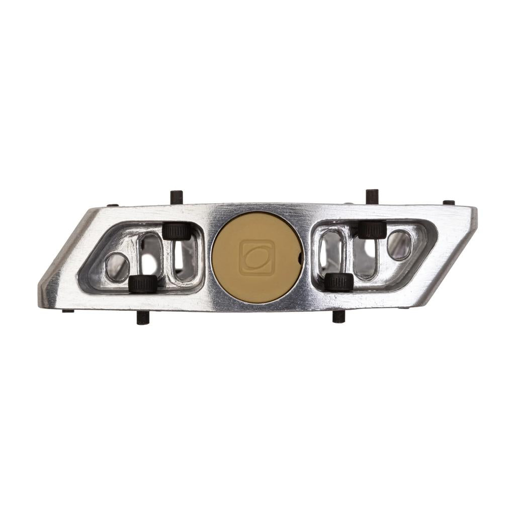 The Odyssey Trail Mix Loose Ball Pedals feature a metallic rectangular aluminum body with a central tan circular part and symmetrical black and silver accents, closely resembling the design of a platform pedal.
