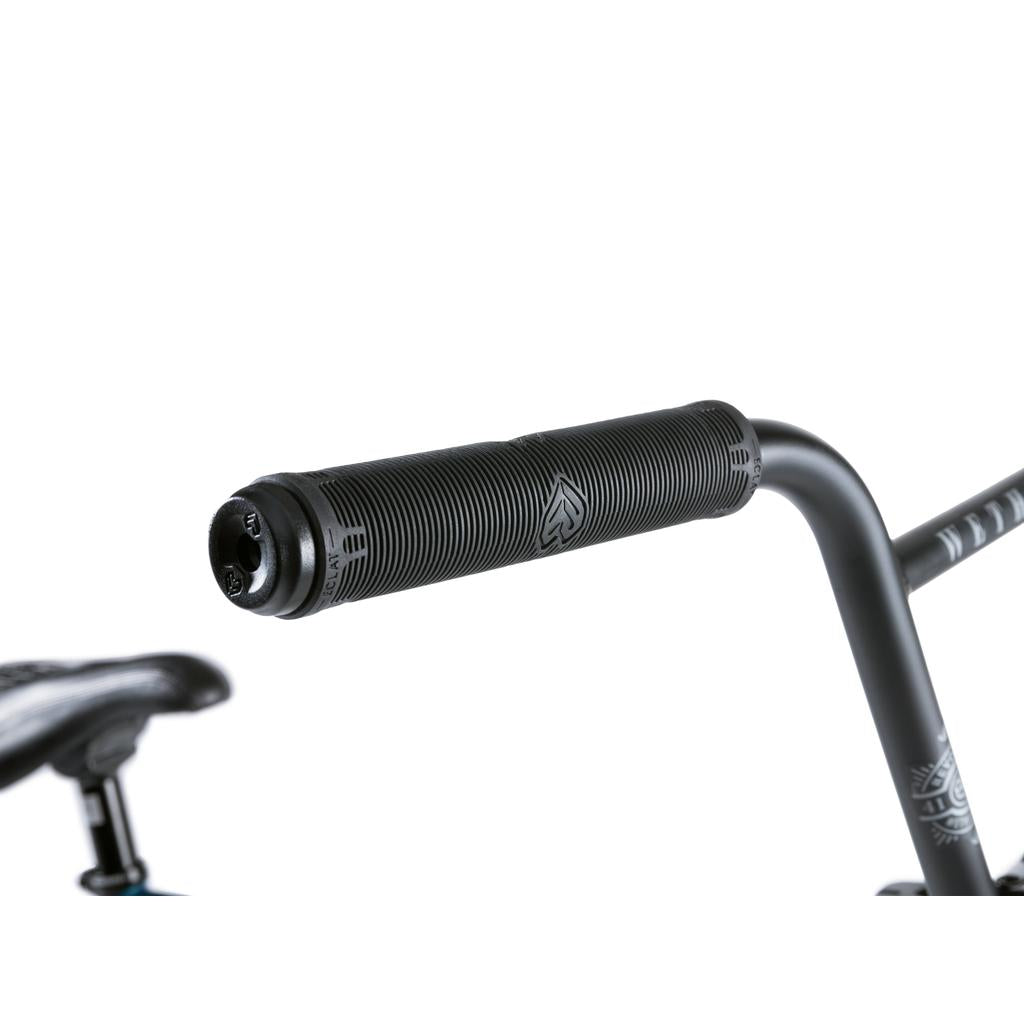 Close-up of a black handlebar grip with textured lines and a logo, part of the Wethepeople Revolver 20 Inch Bike, with a partially visible bicycle seat in the background.
