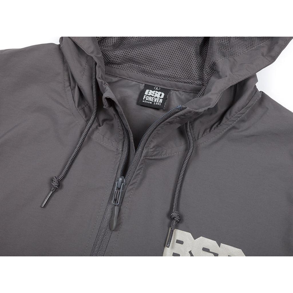 Close-up of a gray BSD Athletic 91 Windbreaker Jacket made of nylon, featuring water resistance, drawstrings, zipper, mesh lining, and a label that reads "RND FOREVER Since 1981.