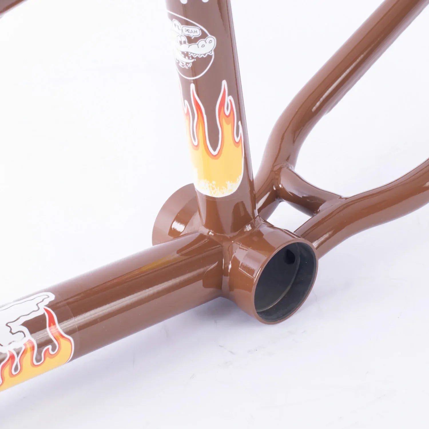 Close-up of a brown Cult Trey Jones Frame with flame decals and stickers, focusing on the bottom bracket area and chainstay junction, set against a white background.