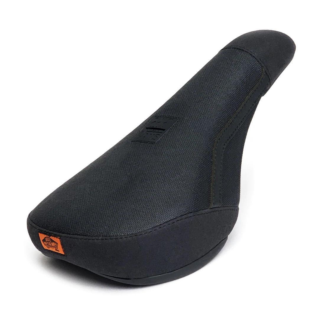 The Cult X Vans Old Skool Pro Pivotal Seat is a black, padded BMX seat with a textured fabric cover, an upward-angled rear, and an orange logo tag on the front left corner—combining style and comfort for your ride.