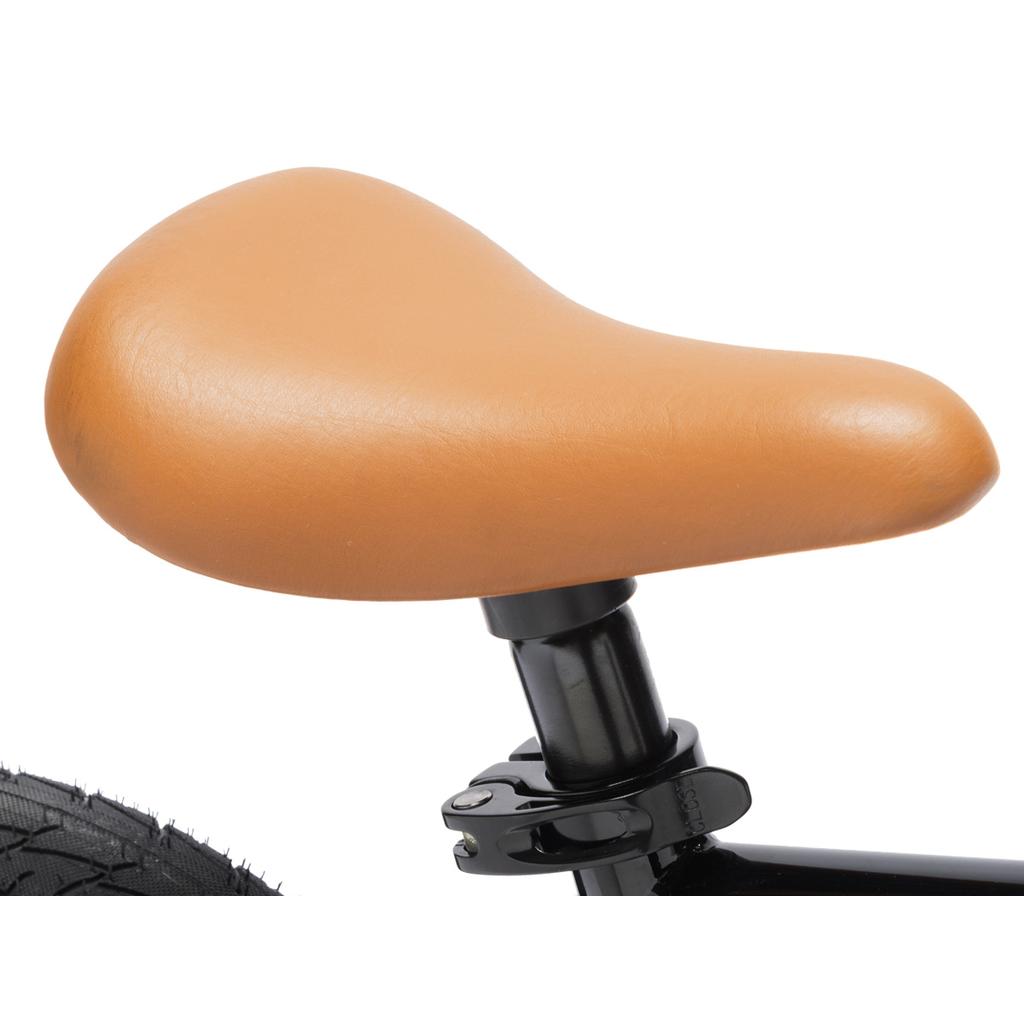 Close-up of the Fit Misfit 12 Inch Bike’s brown seat on a black post, with part of the tire visible—ideal for kids’ first pedal bike.