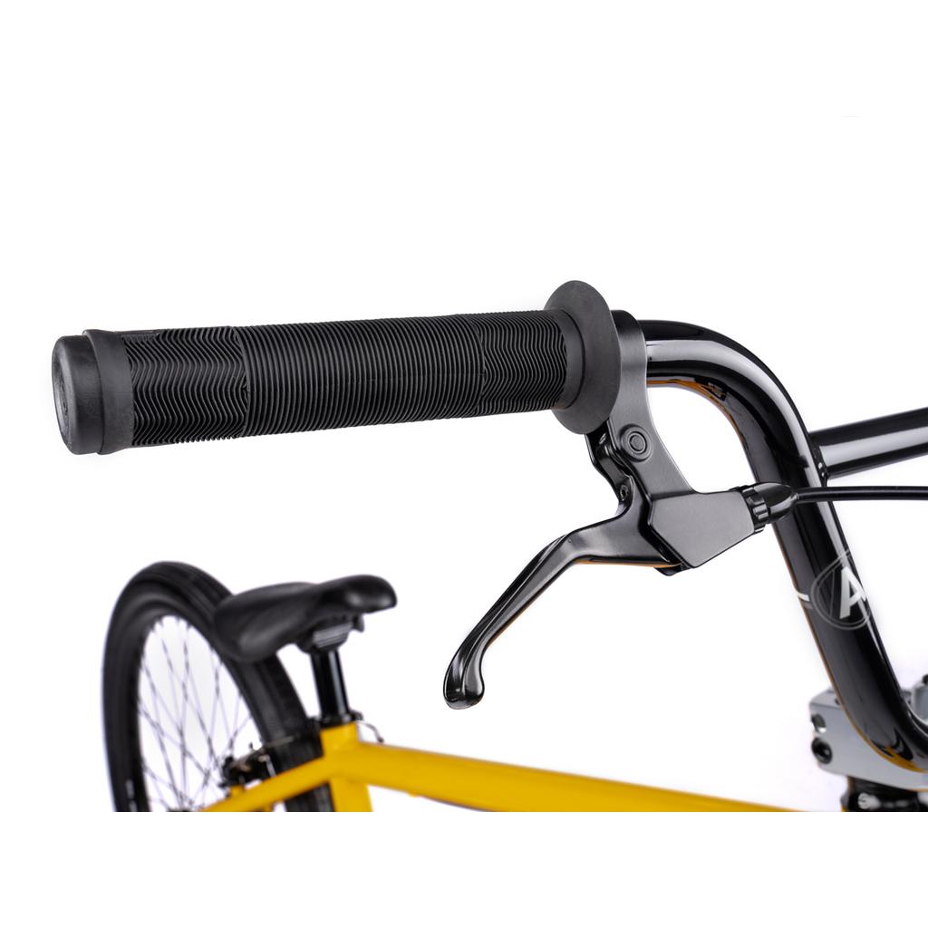 Close-up of the Wethepeople Atlas 24 Inch Bike's black handlebar and brake lever, with part of its yellow frame, black seat, and rear wheel visible against a white background.