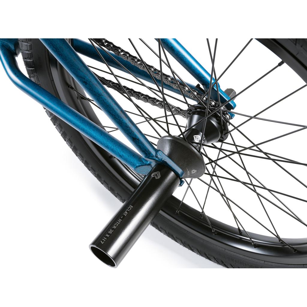 Close-up of a Wethepeople Revolver 20 Inch Bike's rear wheel, displaying the chain, spokes, tire, and a black metal axle peg attached to its blue frame.