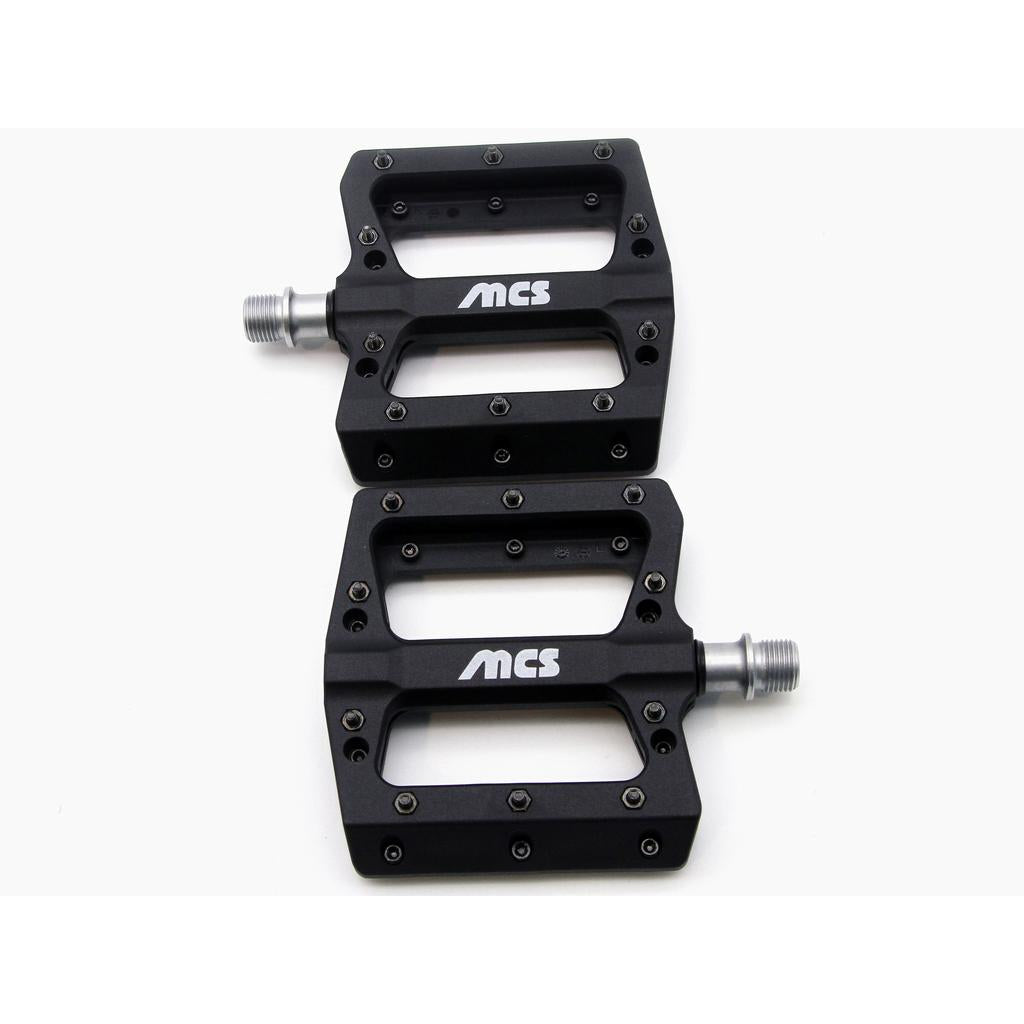 A pair of black MCS Sealed Pedals with silver axles, rectangular shape, and multiple grip pins are shown side by side on a white background.