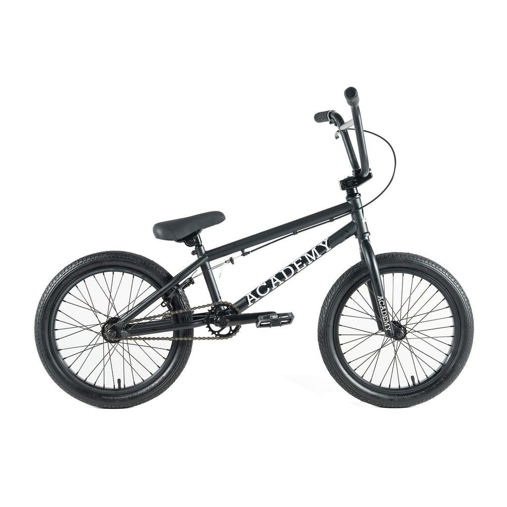 The Academy Inspire 18 Inch Bike features thick tires, straight handlebars, and "ACADEMY" printed on the black frame. Shown from the side on a white background.