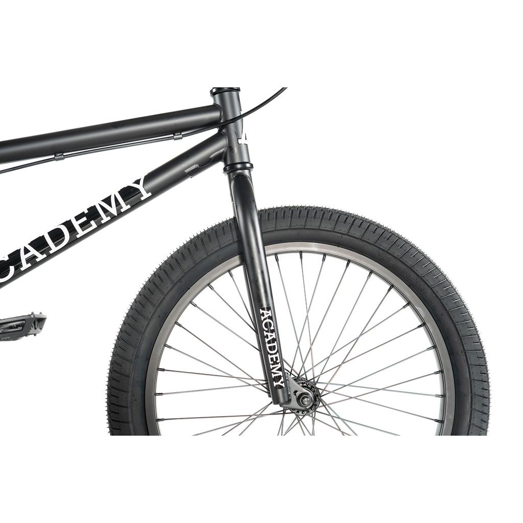 Close-up of the front half of a black Academy Trooper 20 Inch Bike with tire, spokes, pedals, and "ACADEMY" printed on the frame and fork—perfect for beginner BMX riders.