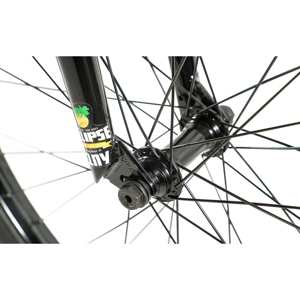 Close-up of the Colony Eclipse 26 Inch Bike’s black front wheel hub, spokes, and fork with a sticker—showcasing axle and bolt details on a white backdrop. The chromoly frame offers durability for every ride.