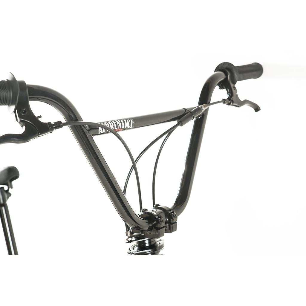 Close-up of black flatland BMX handlebars with brake cables, brake lever, and "APPRENTICE" branding on the crossbar, featured on the Colony Apprentice Flatland 20 Inch Bike with an 18.9" frame.