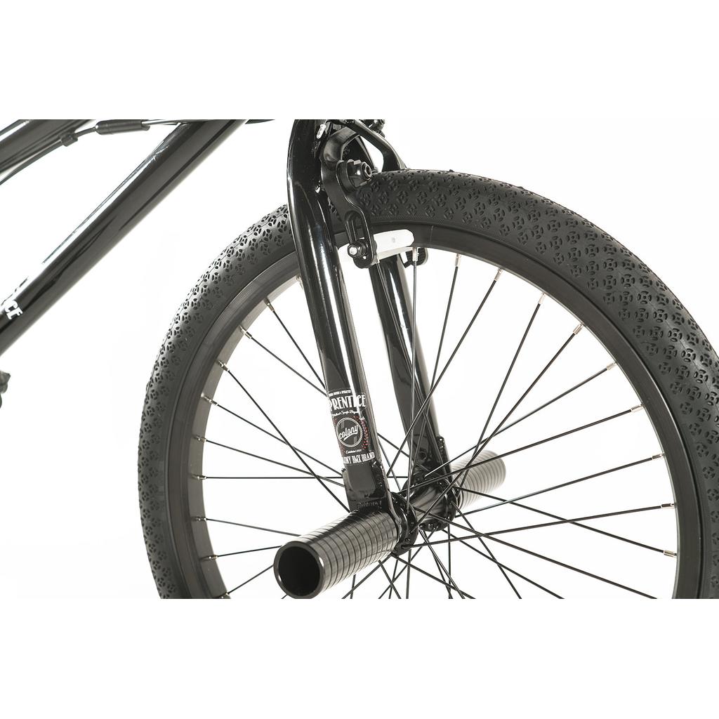 Close-up of the Colony Apprentice Flatland 20 Inch Bike’s black front wheel with thick tire, metal pegs, fork, and spokes on a white background—ideal for flatland BMX riders seeking a pro-level 20" bike.