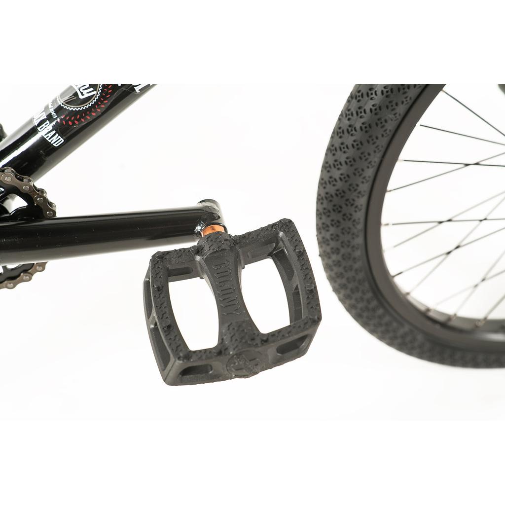 Close-up of a bicycle pedal attached to a black crank arm, with part of the rear wheel and tire visible—perfect for riders of the Colony Apprentice Flatland 20 Inch Bike, featuring an agile frame built for flatland BMX tricks.