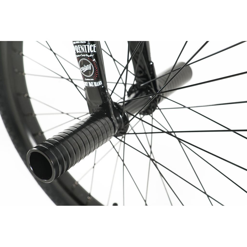 Close-up of a Colony Apprentice Flatland 20 Inch Bike front wheel, featuring black spokes and a metal peg on the axle—ideal for flatland tricks and perfect for BMX riders.