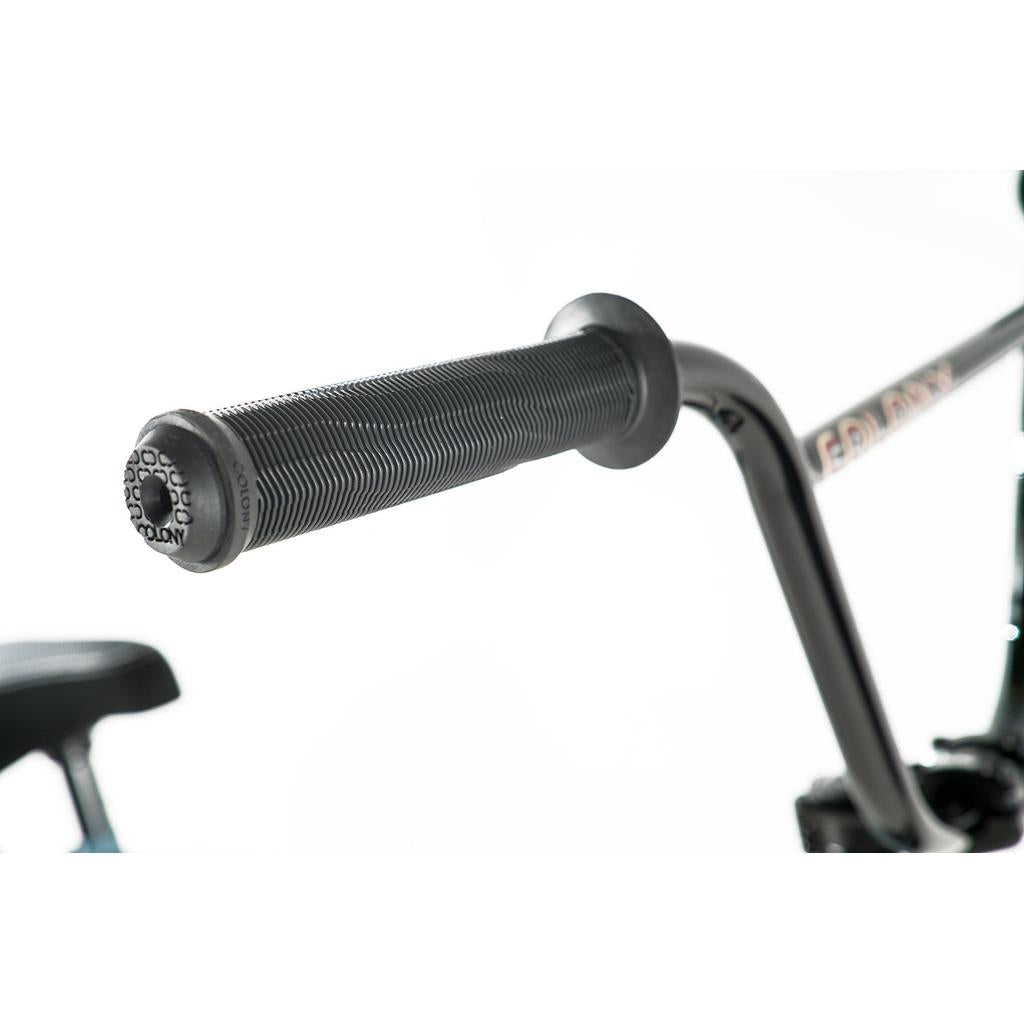 Close-up of the Colony Emerge 20 Inch Bike’s handlebar with a textured black rubber grip, featuring signature Colony BMX details, and part of the seat visible in the background.