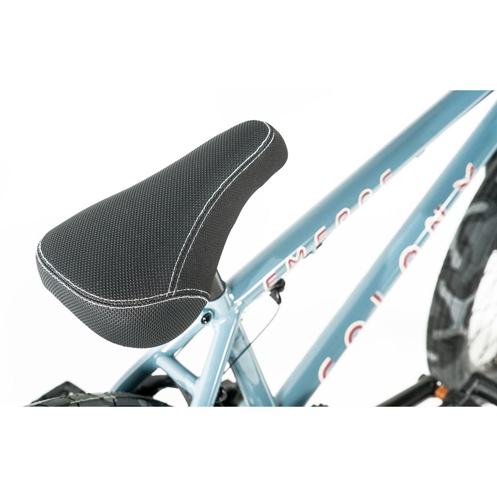 Close-up of a black bicycle seat with white stitching on a light blue Colony Emerge 20 Inch Bike frame, partially showing the word "EMERGE" and the rear tire.