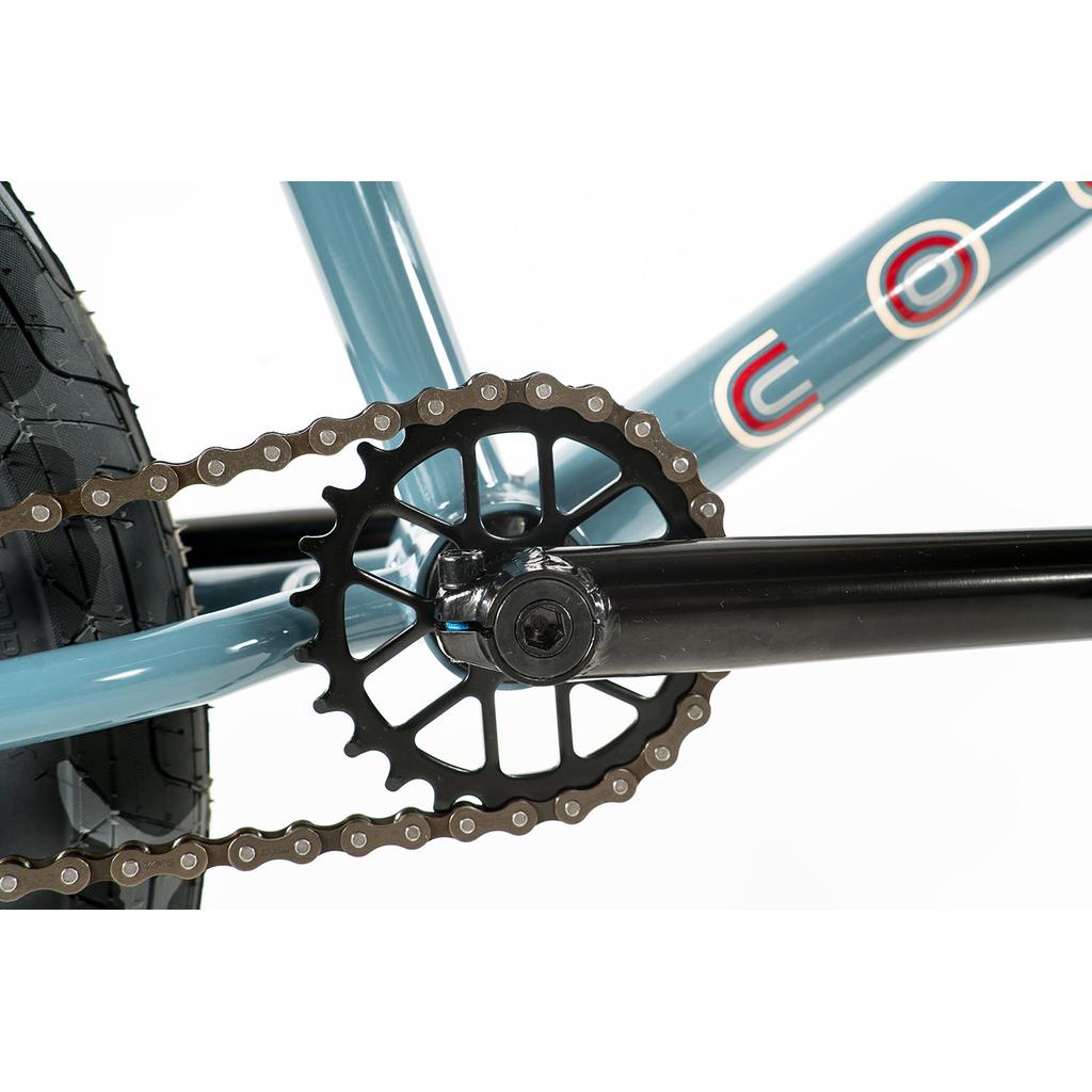 Close-up of the crankset, chainring, and chain on a blue Chromoly frame with part of a tire—highlighting the Colony Emerge 20 Inch Bike's durable BMX construction.