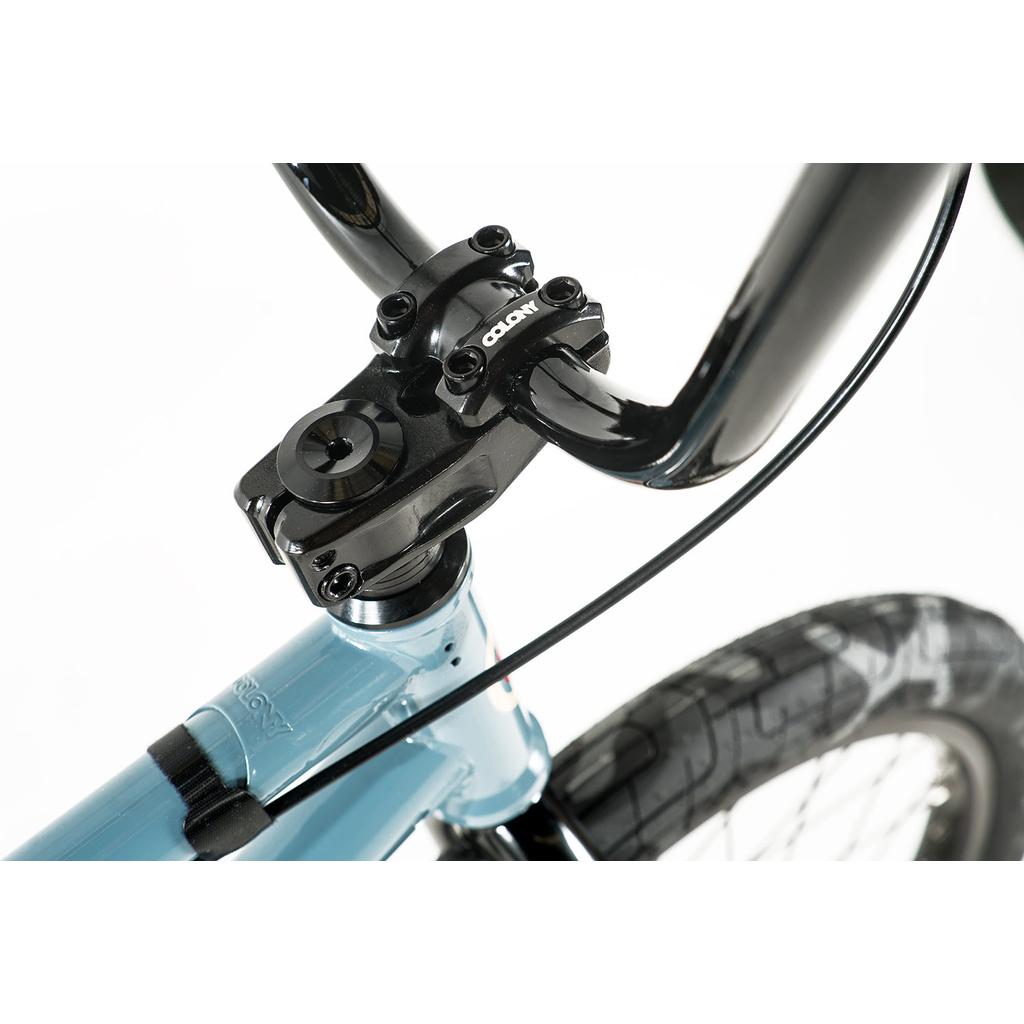 Close-up of the Colony Emerge 20 Inch Bike's black handlebar and stem on a light blue Chromoly frame, showing the front tire and brake cable.