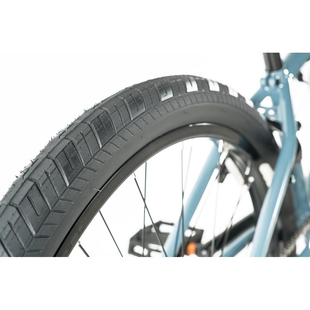 Close-up of a black tire and part of the blue Colony Eclipse 24 Inch Bike chromoly frame, showcasing the tread pattern and spokes against a white background.