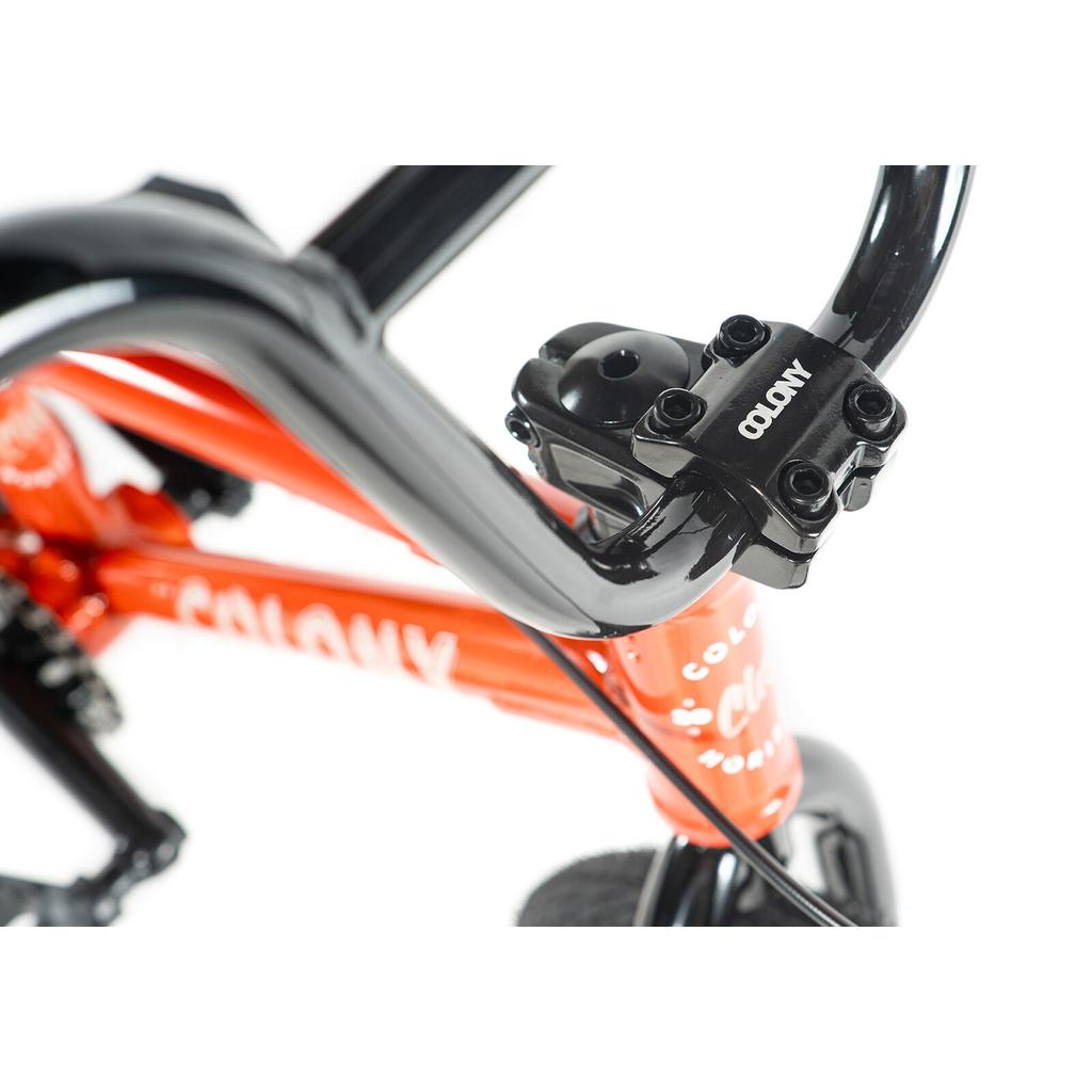 Close-up of a Colony Horizon 14 Inch Bike’s black handlebars and stem with "Colony" branding, attached to an orange lightweight alloy frame featuring a partial "Colony" logo.