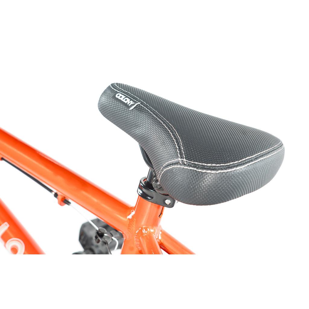 Close-up of a black bike saddle with white stitching on an orange Colony Horizon 16 Inch Bike frame, shown against a white background.