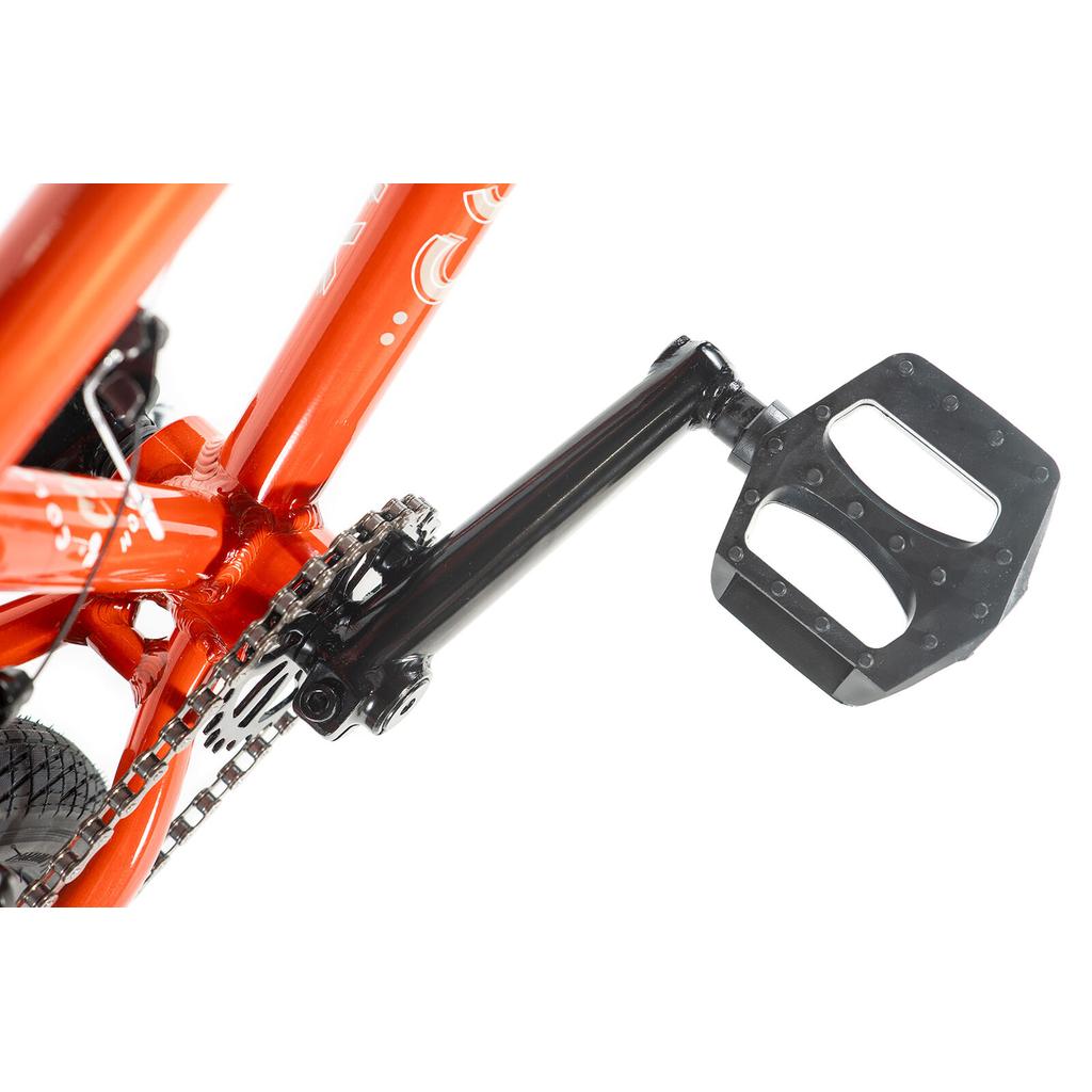 Close-up of a black pedal and crank arm attached to an orange Colony Horizon 18 Inch Bike frame, with part of the chain and rear tire visible.