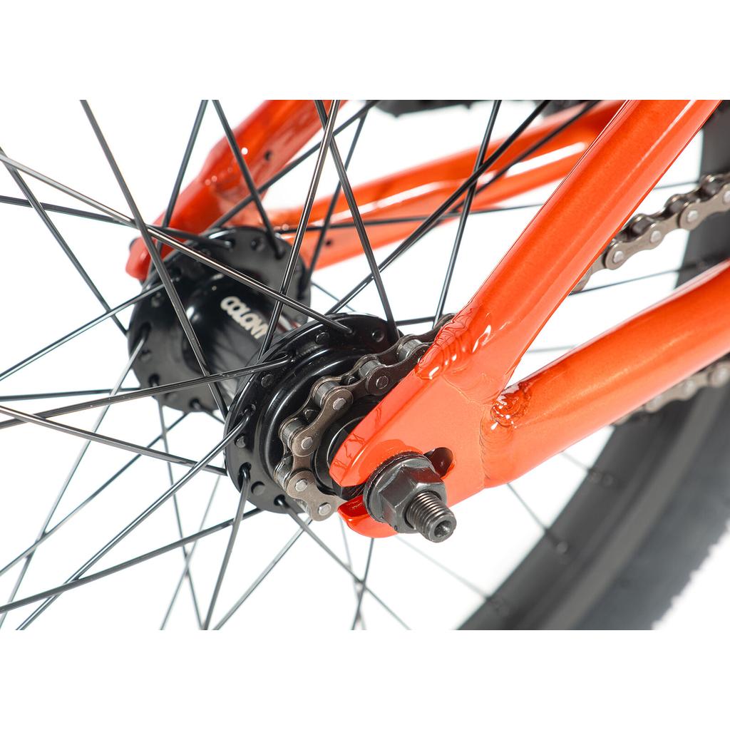 Close-up of the Colony Horizon 18 Inch Bike's rear wheel hub with black spokes, chain, and an orange frame—ideal for any aspiring freestyle Olympic athlete.