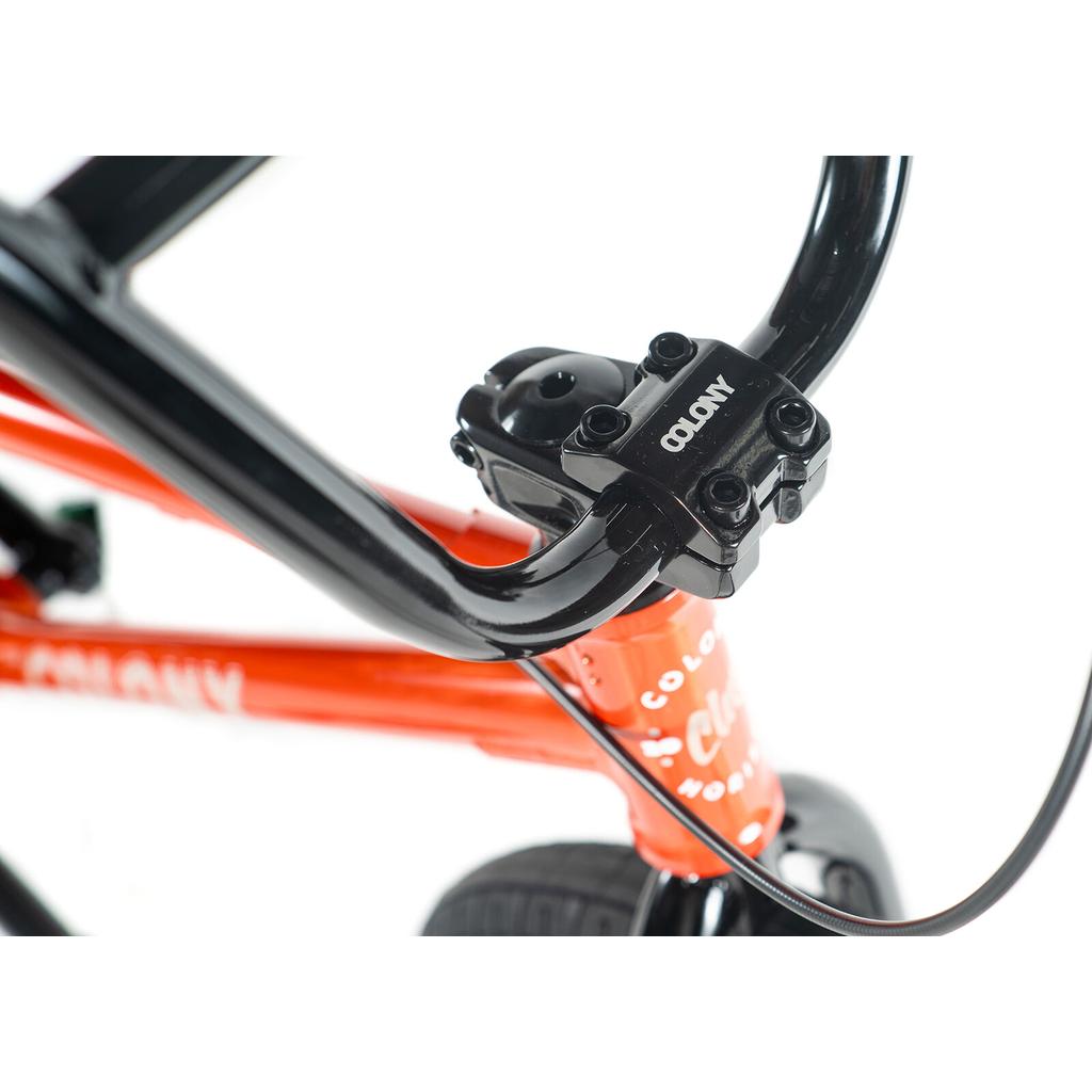 Close-up of the handlebars, stem, and front frame of the Colony Horizon 20 Inch Bike in orange, featuring black handlebars and a front brake cable—highlighting its BMX Freestyle design.