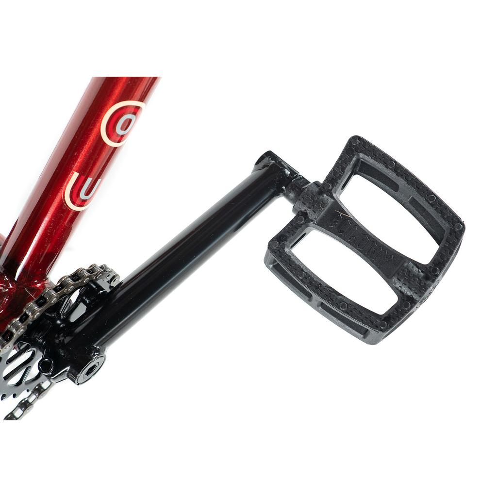 Close-up of the colony-emerge-bike-2020's black pedal and crank arm attached to its red frame, showing the chainring and chain.