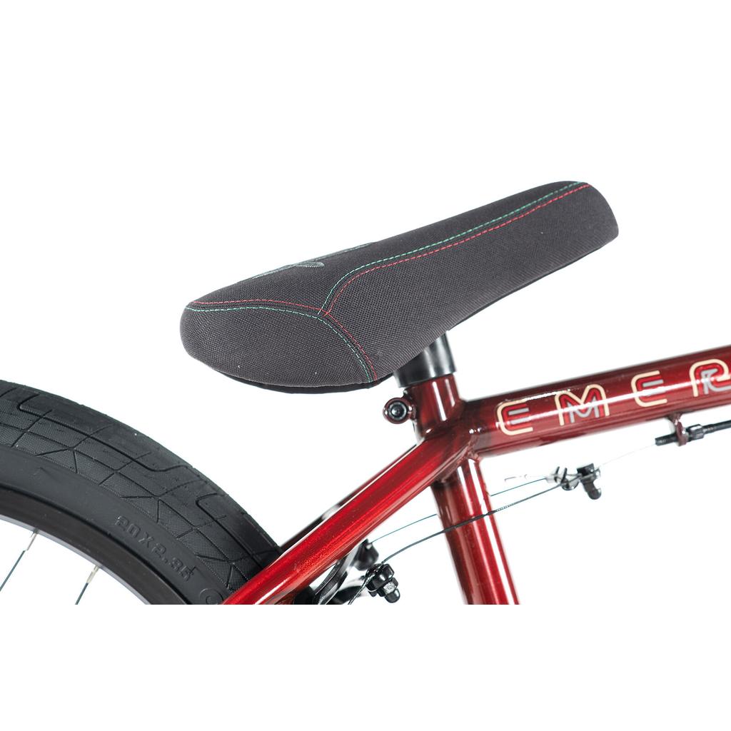 Close-up of the colony-emerge-bike-2020’s black seat with colored stitching on its red frame, showing part of the rear tire and seat post.