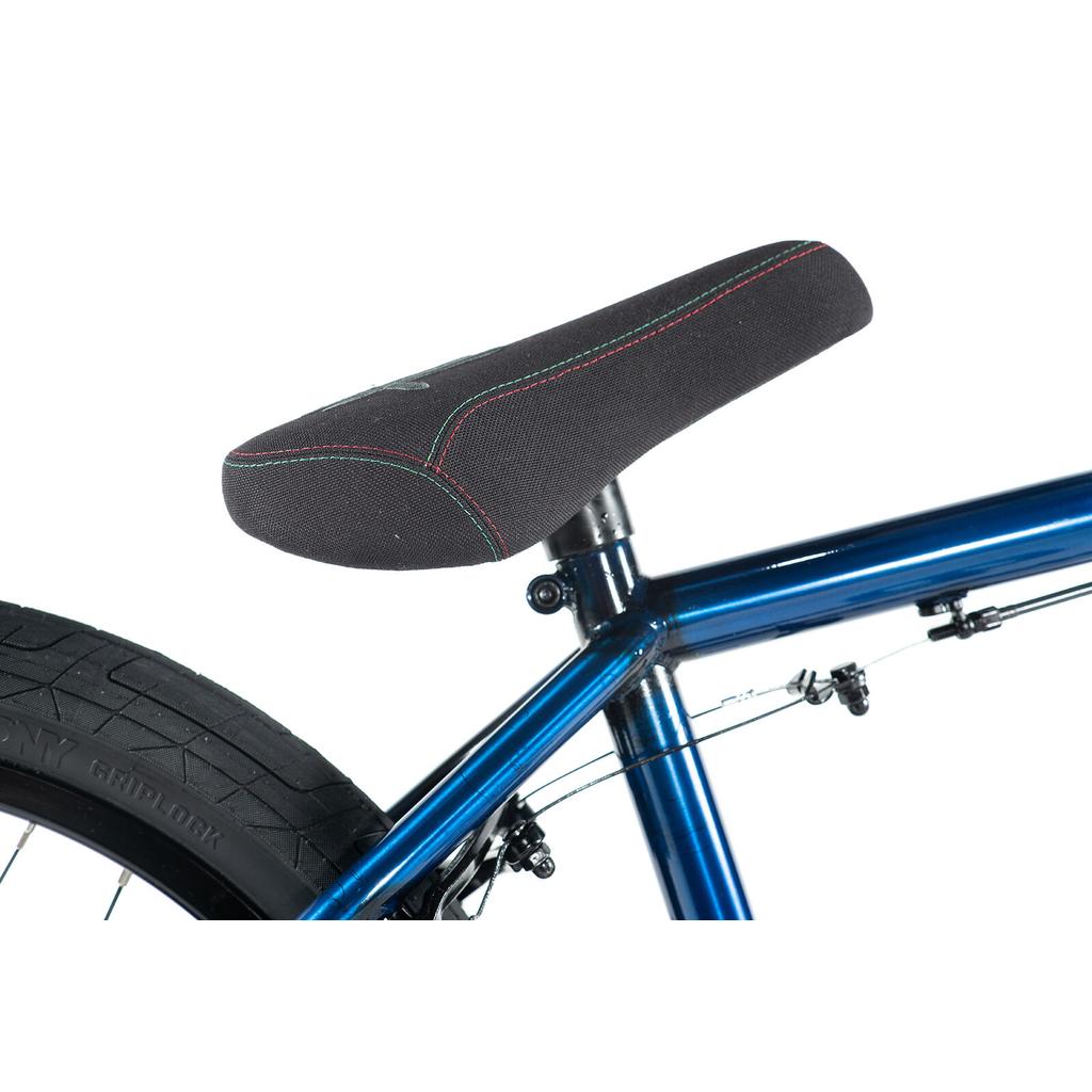 Close-up of a black bicycle seat with colored stitching on the Colony Premise 20 Inch Bike’s blue chromoly BMX frame, showing rear tire and brake cables.