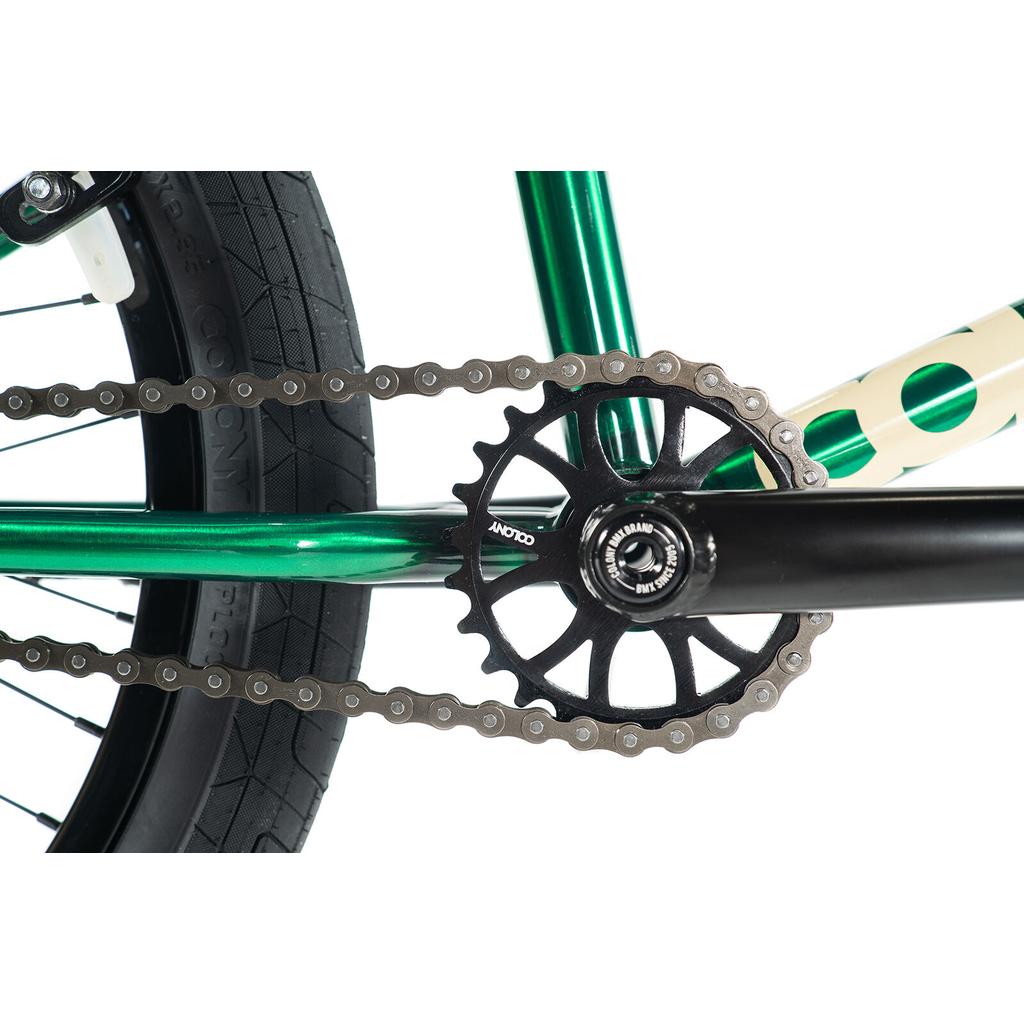 Close-up of the Colony Cadet Elite 20 Inch Bike's rear wheel, chain, and green frame, highlighting the chainring, crank arm, and tire tread details on this pro-level BMX with full CrMo construction and stable geometry.