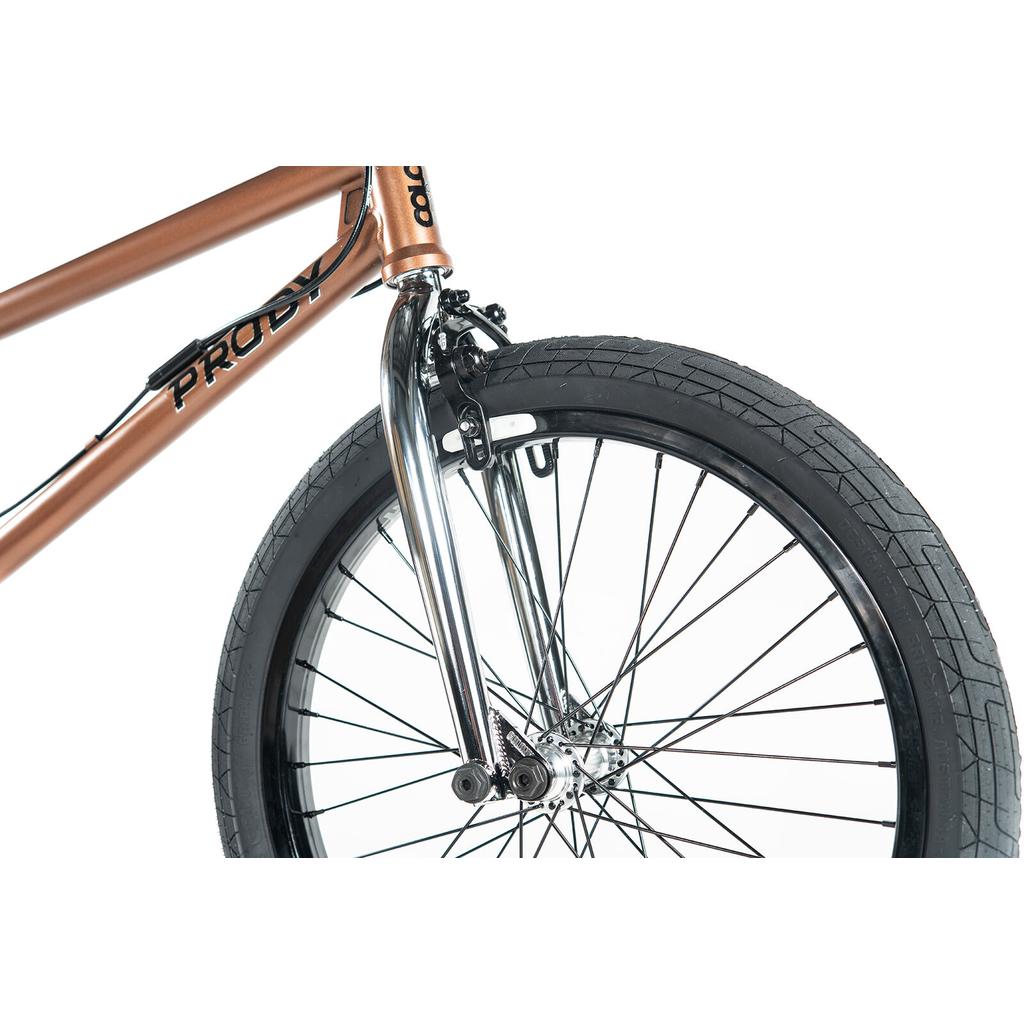 Close-up of the front wheel and fork of a Colony Prody Elite 20 Inch Bike, showing a bronze CrMo frame, black tire, and silver spokes against a white background.